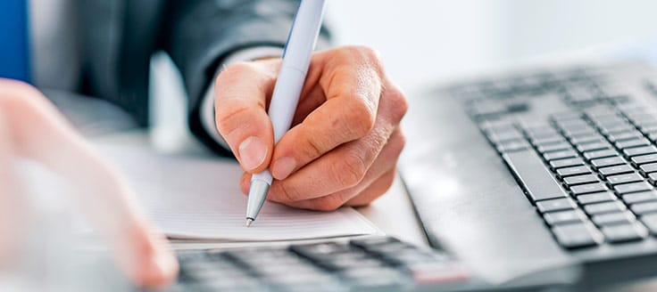 A man works at a desk as he writes figures on his small business’s financial report.