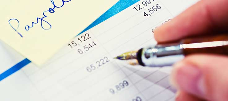 A person uses a pen to make manual corrections to payroll. An automated payroll service can help your small business.