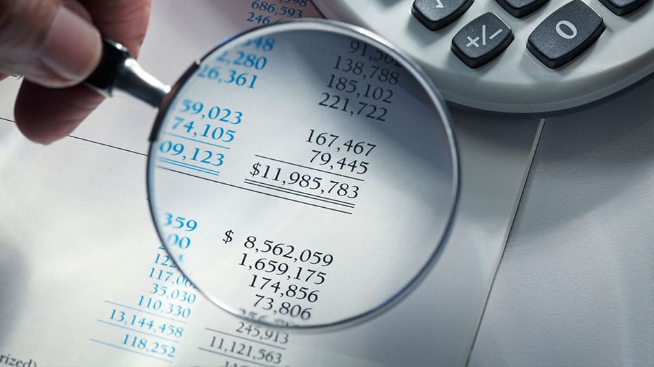 A magnifying glass hovers over numbers on a balance sheet. Learn the relationship between assets, liabilities and equity.