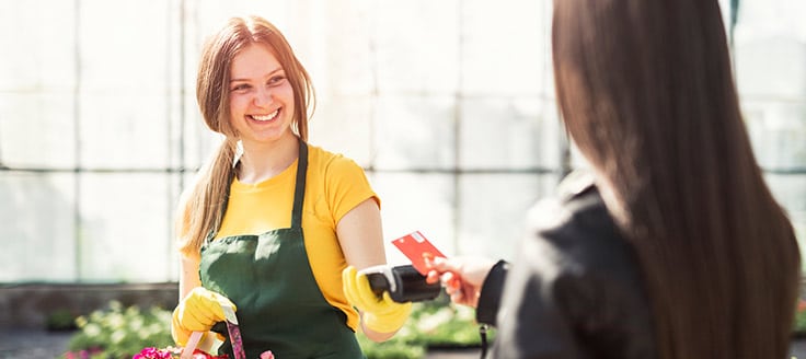 A nursery owner scans a customer’s credit card with a mobile device. A business merchant account helps you automate accepting credit and debit cards.