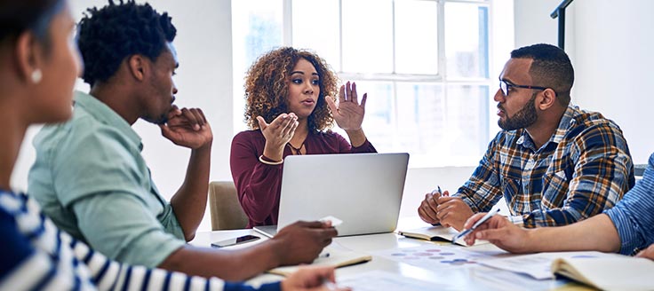 Co-workers hold a meeting at a conference table, perhaps discussing QuickBooks online vs. desktop and which is best for their business.