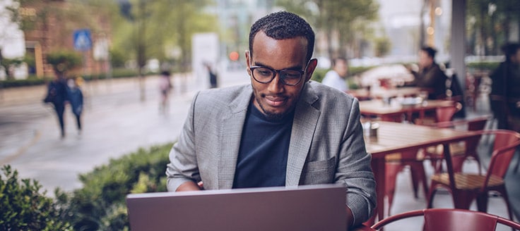 A man works on his laptop as he sits at an outdoor cafe.