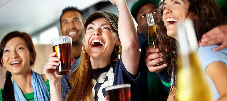 A group of people huddle together as they enjoy beer at a bar. Your on-premise liquor license can allow you to serve alcoholic beverages to customers.