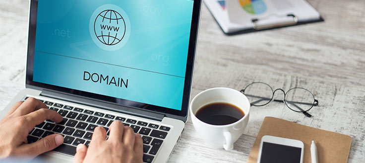 A businessman sits at a desk and types at a laptop to obtain a free domain name.