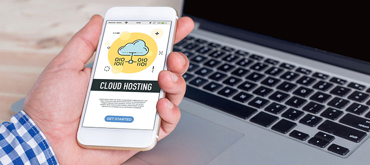 A man looks at a cloud-hosting program on his smartphone while he sits in front of his laptop.