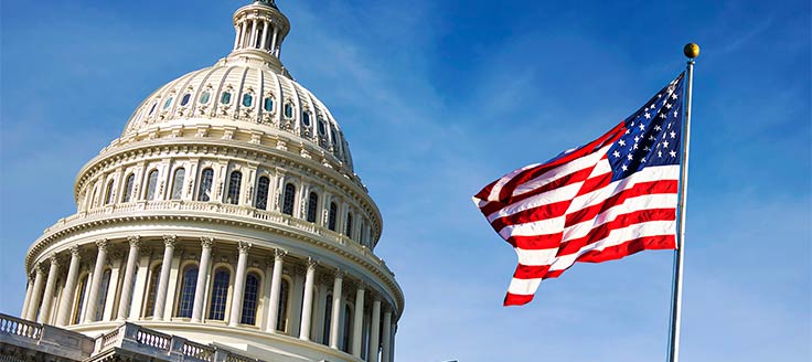 The U.S. Capitol building with an American flag in the foreground and a blue sky in the background.