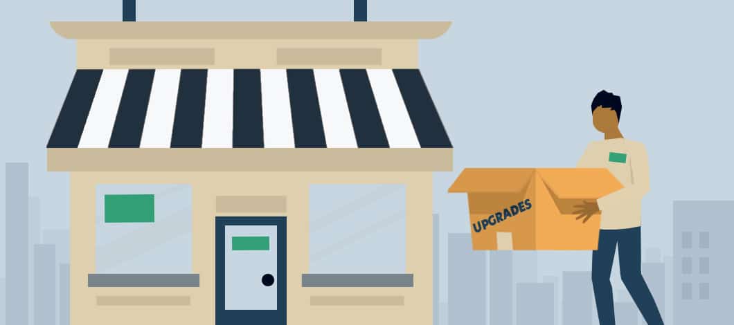 A small business owner carries a box labeled “Upgrades” into his small shop.