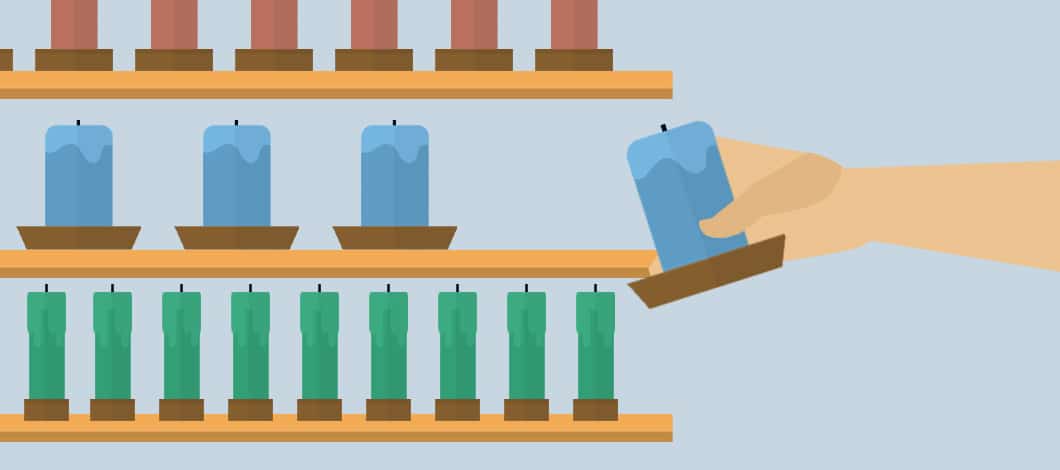A hand places a blue candle on a store shelf that has other blue candles. The shelf above is filled with red candles and the shelf below has green candles.