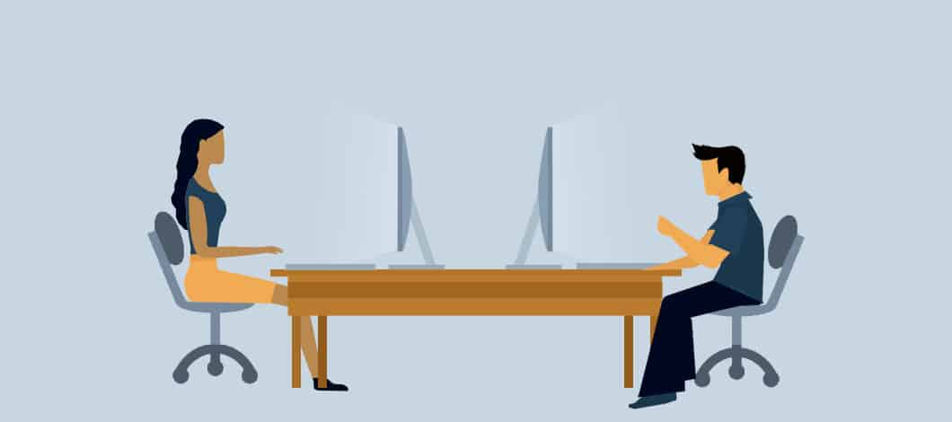 A business couple sits across from each other at a table, working on their laptops.