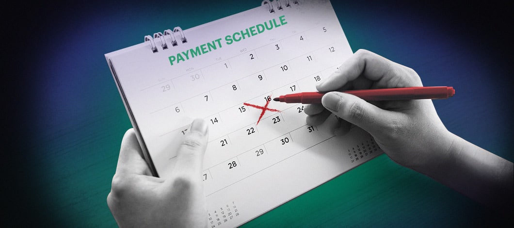 A hand with a marker draws an “X” on one of the days of a calendar page labeled “Payment Schedule.”